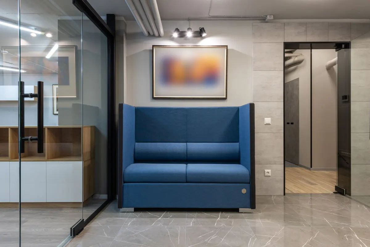 Office reception area with a blue sofa, glass partition and tiled floor.